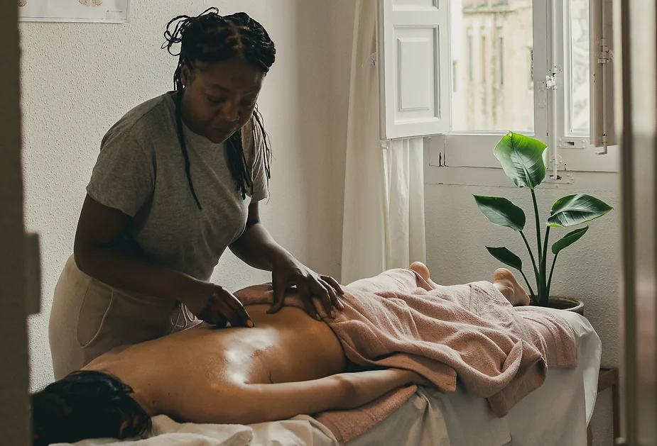 A massage therapist working on a client's back in a serene room with natural light coming in through the window, performing a Relaxing Holistic Massage.