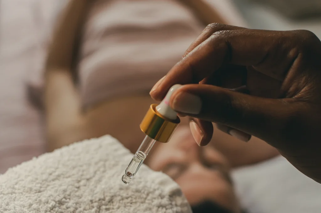 A close-up of a person receiving an anti-cellulite facial, with one hand using a dropper to apply a liquid to the face.