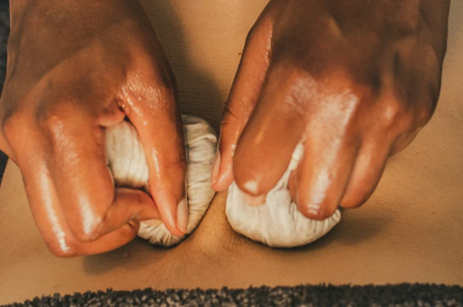 Two hands kneading dough on a wooden surface, showing a close-up view of the dough squeezing between the fingers, reminiscent of massage techniques.