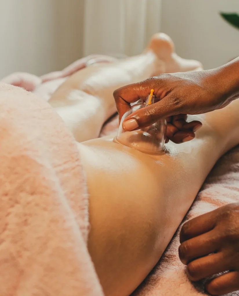 A person receives an anti-cellulite cupping therapy treatment on their back, with a practitioner's hands applying a cupping cup to their skin. The setting appears calm, with a soft-focus background.