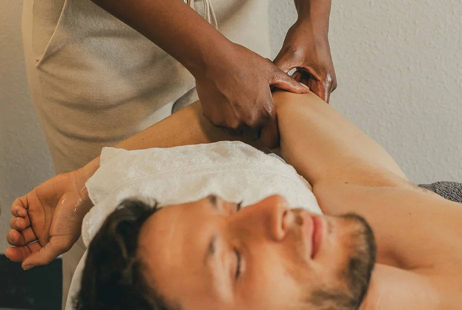 A masseuse provides a soothing arm massage to a smiling man lying on a massage table, conveying a serene and relaxing atmosphere.