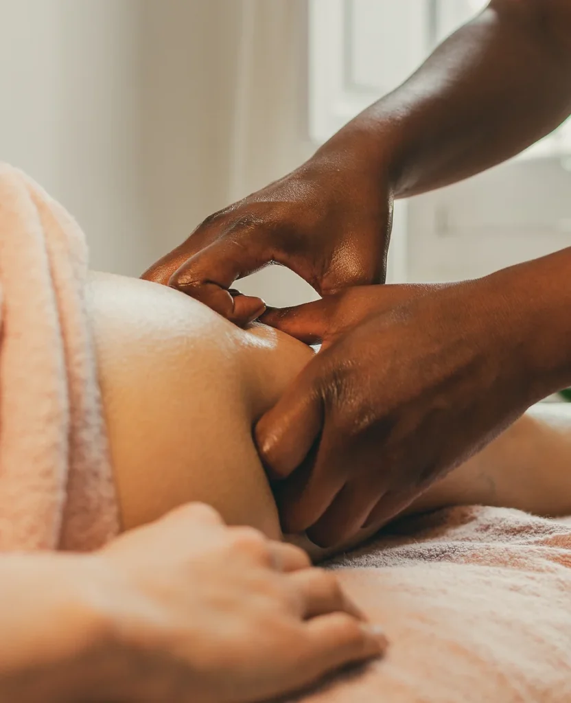 Close-up of a therapeutic massage session focused on a person's shoulder, with a therapist's hands applying anti-cellulite pressure to the muscle.