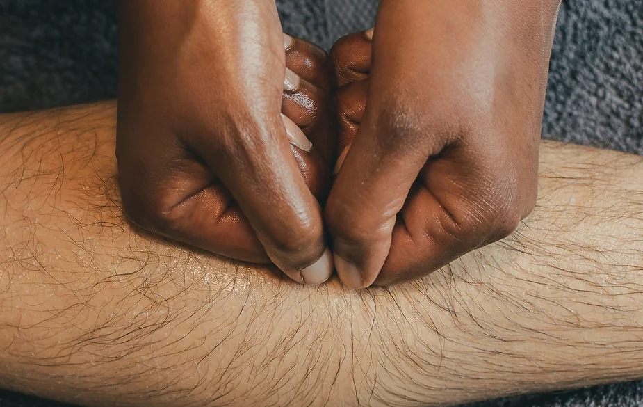 Close-up of a physical therapist's hands applying pressure to a patient's calf muscle, emphasizing Indonesian massage techniques.