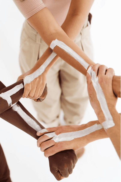 A group of hands, of various skin tones, joined together to form a square using white ribbon, symbolizing unity and teamwork through collaborations. The background is clean and white.