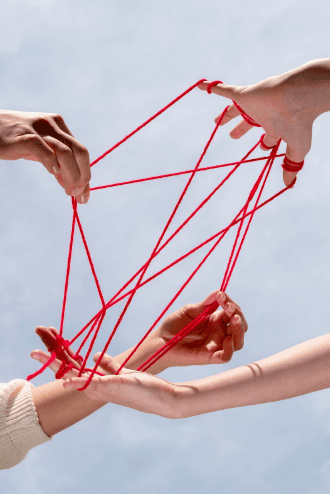 Four hands manipulate a red thread to form a complex web against a clear sky background, symbolizing collaborations and teamwork.