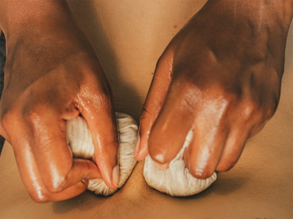 Close-up photo of two hands kneading on a wooden surface, highlighting the detailed texture of the pindas and skin.