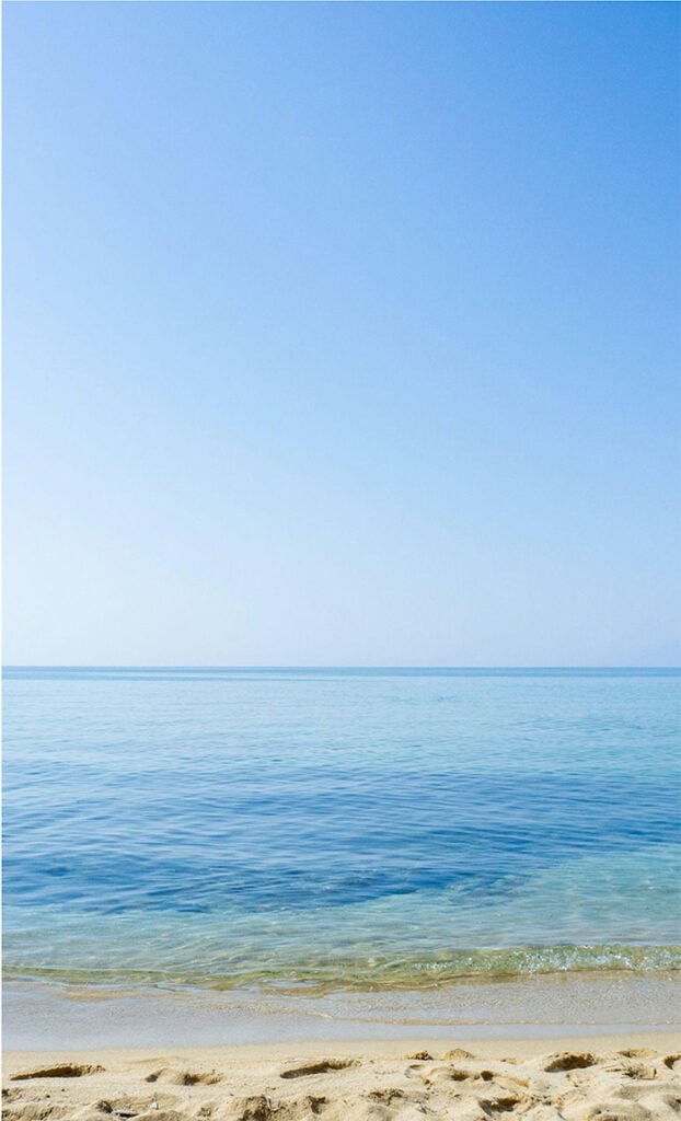 Una serena vista al mar con un cielo azul claro, aguas turquesas tranquilas y suaves olas rompiendo contra una playa de arena. El horizonte se funde a la perfección entre el mar y el cielo, creando una escena tranquila y pacífica que recuerda a un boceto de un borrador automático.