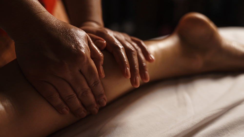 Una persona recibe un masaje en las piernas después de correr, con dos manos presionando y amasando suavemente un muslo sobre una mesa de masaje suavemente cubierta, creando una atmósfera relajante y tranquilizadora que recuerda a las serenas calles de Valencia.